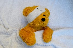 Sick Teddy laying in bed, with a bandage across his head